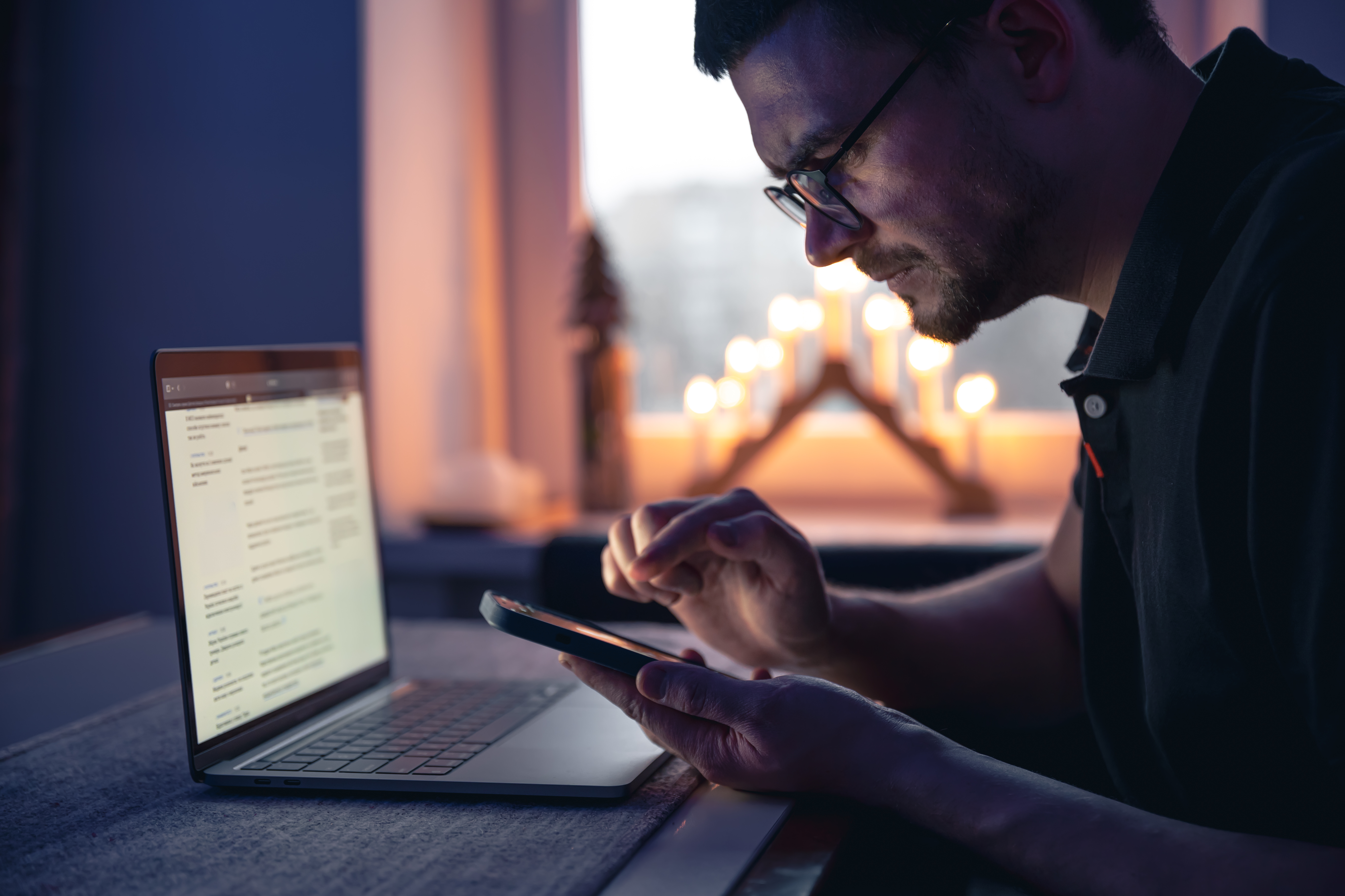 man with smartphone sits front laptop late night